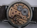 Close-up view of a watch's intricate mechanical movement, showing brass plates, silver gears, and ruby jewels. Engravings "OMEGA WATCH Co SWISS", "SEVENTEEN 17 JEWELS", and "ADJUSTED TWO (2) POSITIONS" are visible.