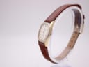 Angled side view of the Omega De Ville watch, showing the gold-plated case side and brown leather strap.