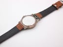 View of the watch's stainless steel case back and the extended brown leather strap, showing its underside.