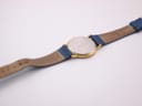 View of the watch from the back, showing the case back and the underside of the blue leather strap.