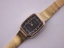 Angled top-down view of the Tissot rectangular gold-tone watch with a black dial and mesh bracelet.