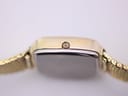 Close-up of the small, unmarked crown on the side of the gold-tone watch case.