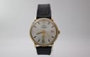 Front view of the Mondaine automatic watch, showing its silver sunburst dial, gold-tone case, and black leather strap.