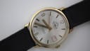 Another angled side view of the Mondaine automatic watch, showing the left profile of the gold-plated case and strap.