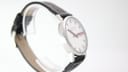 Oblique view of the Mondaine watch highlighting the clean lines of the stainless steel case and the black leather strap with white stitching.