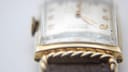 Angled view of the watch on a clear stand, showcasing the distinctive curved case and dial.