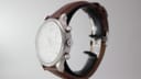 Angled side view of the Tissot watch showing the signed crown, chronograph pushers, and case profile on a display stand.