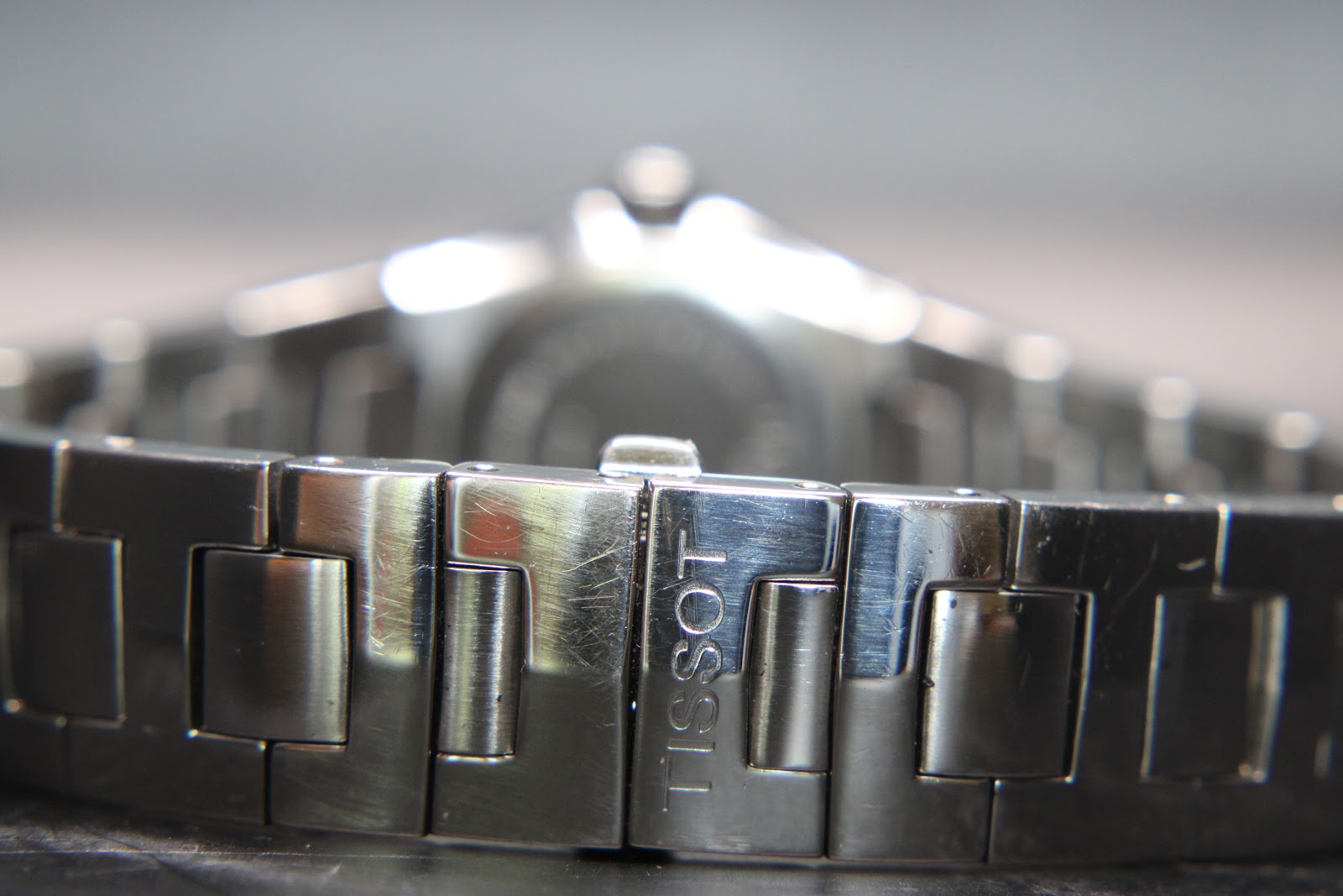 Close-up of the Tissot signed deployment clasp on the stainless steel bracelet, showing light wear marks.