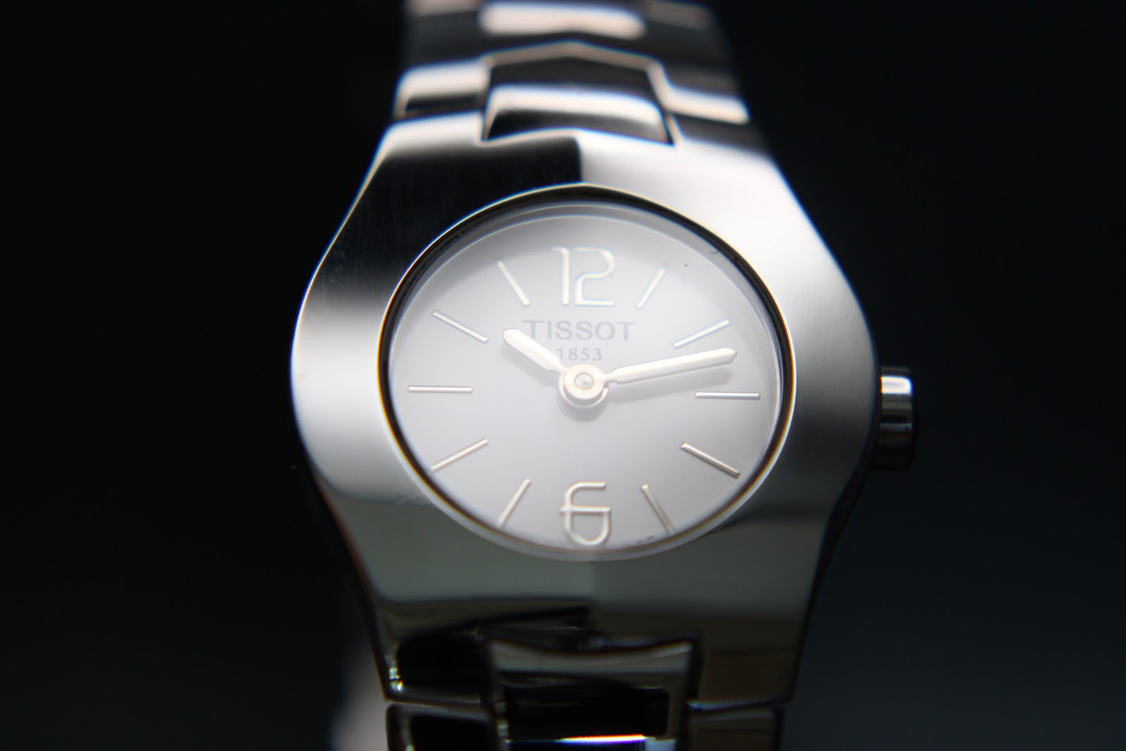 Extreme close-up of the Tissot L520 watch dial, showing "Tissot 1853 Swiss Made" text, raised indices, and a small seconds hand.
