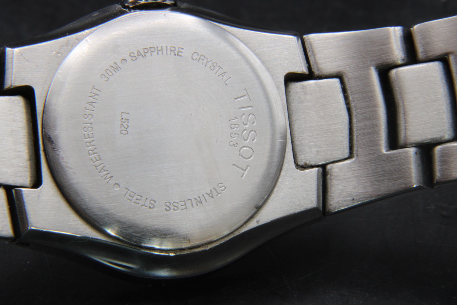 Close-up of the watch case back, engraved with "TISSOT 1853", "STAINLESS STEEL", "WATER RESISTANT 30M", "SAPPHIRE CRYSTAL", and "L520".
