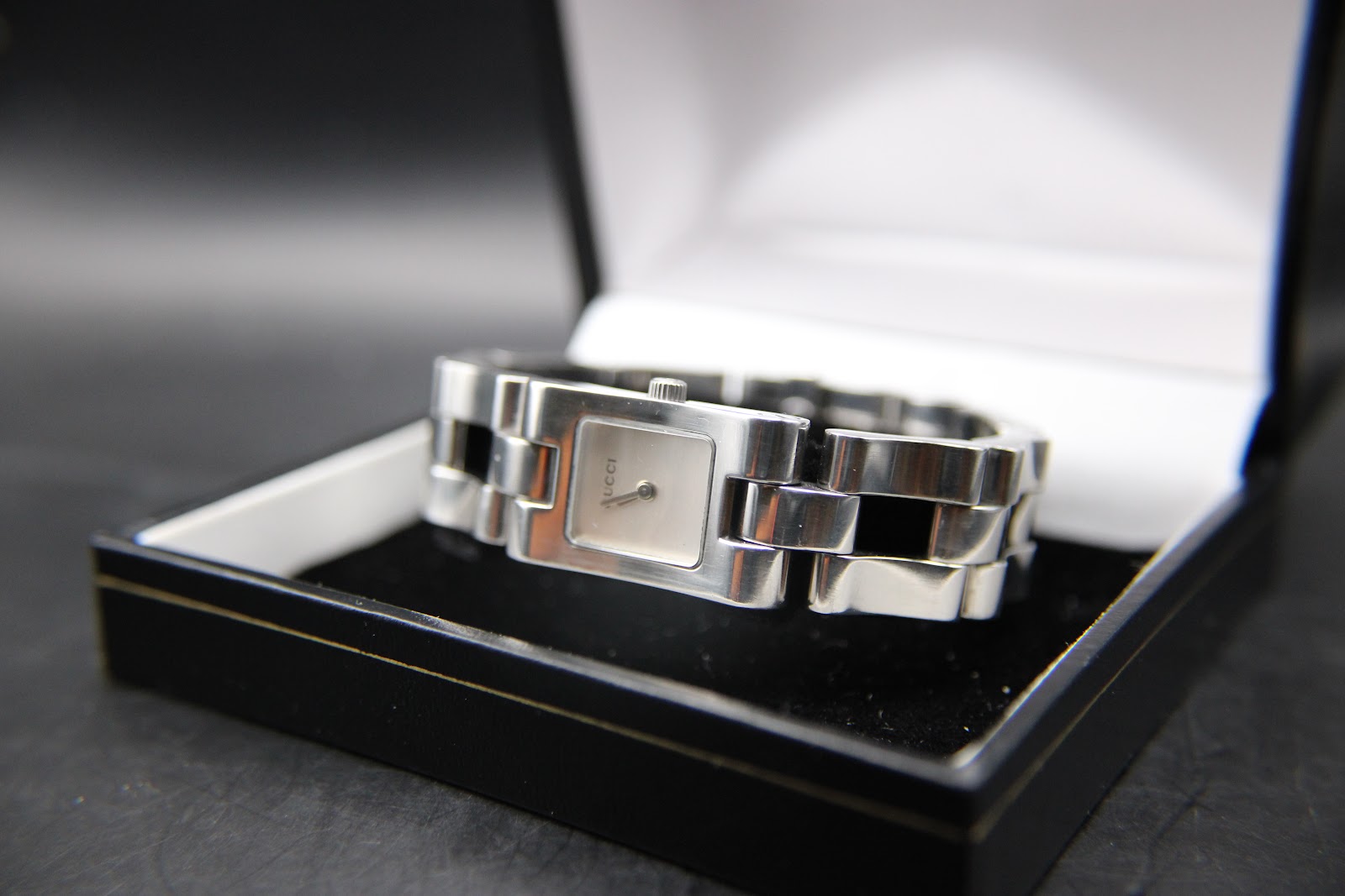 Top-down view of the Gucci 2305L watch, resting in an open black display box, highlighting the square silver dial and polished finish.