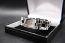 Top-down view of the Gucci 2305L watch, resting in an open black display box, highlighting the square silver dial and polished finish.