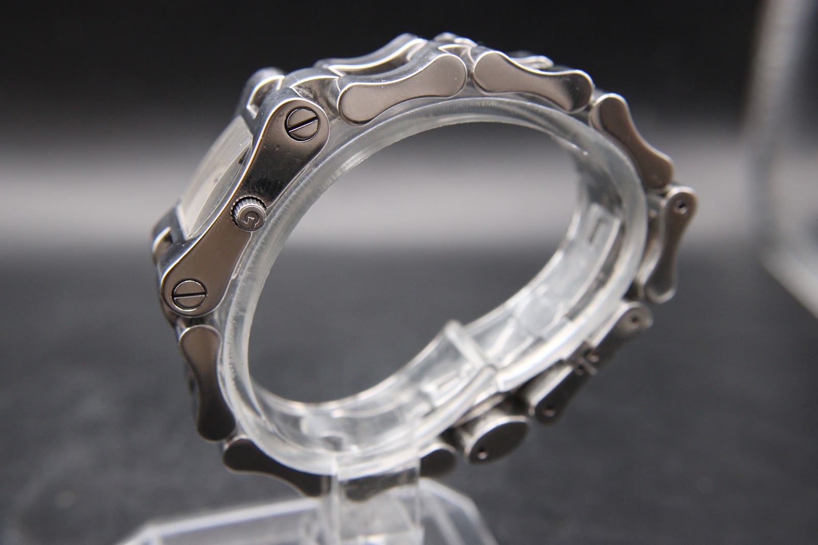 Side view of the Gucci 2305L watch bracelet, showing the unique link design with screws and the watch crown, on a clear display stand.