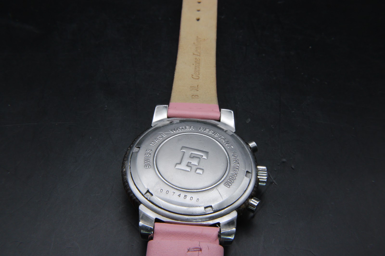 Rear view of the Façonnable watch case back, engraved with 'Swiss Made Water Resistant 10ATM/100M' and serial number 0074508. The 'Genuine Leather 18 XL' inscription on the strap is also visible.