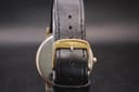 Close-up of the original Longines signed gold-tone buckle on the black leather watch strap.