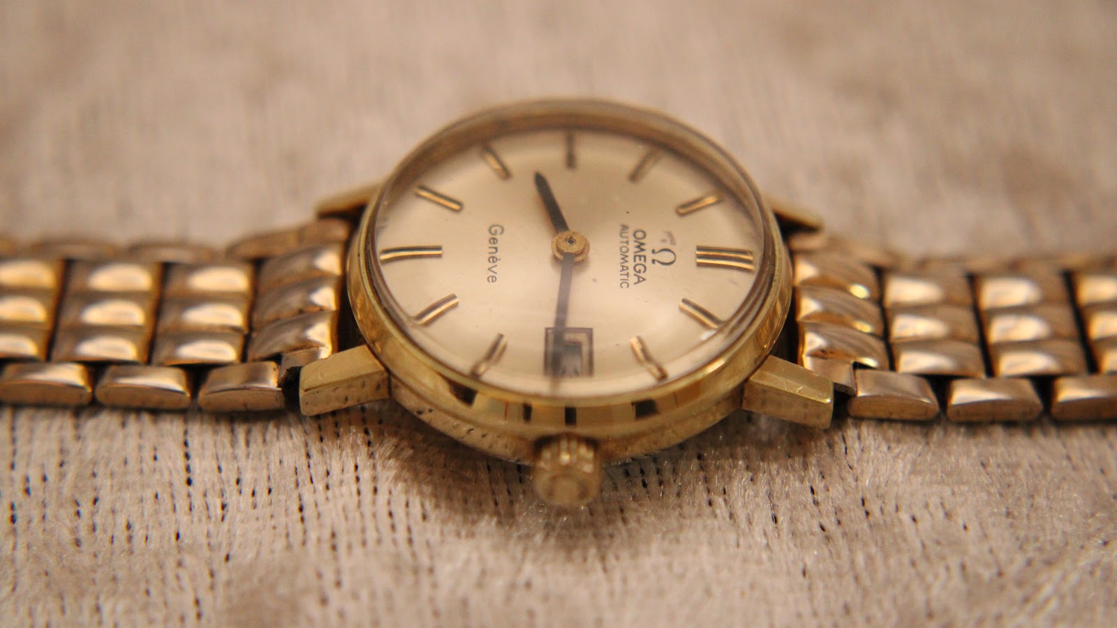 Close-up, slightly angled front view of the Omega Geneve dial, hands, and crown.