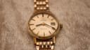 Direct front view of the Omega Geneve automatic watch with champagne dial and gold-tone bracelet on a textured background.