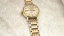 Angled front view of the Omega Geneve watch with champagne dial and gold-tone bracelet on a textured light background.