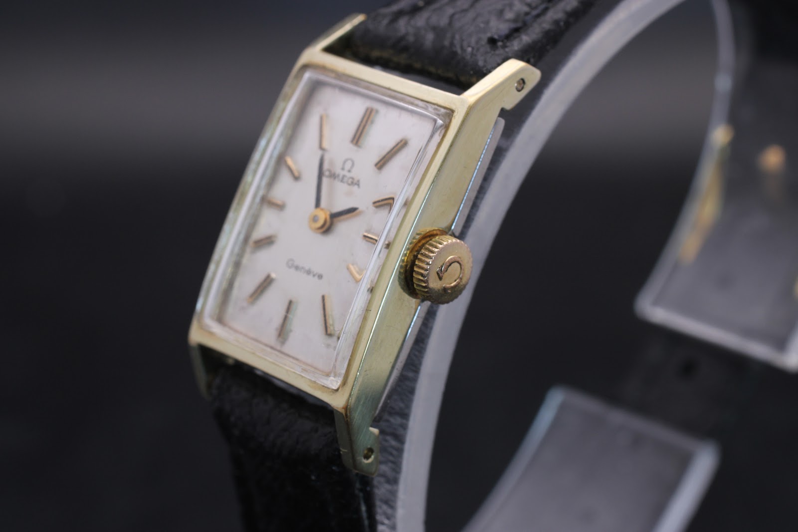 Close-up side view of the Omega Genève watch case and signed crown, showing the gold plating and rectangular shape.