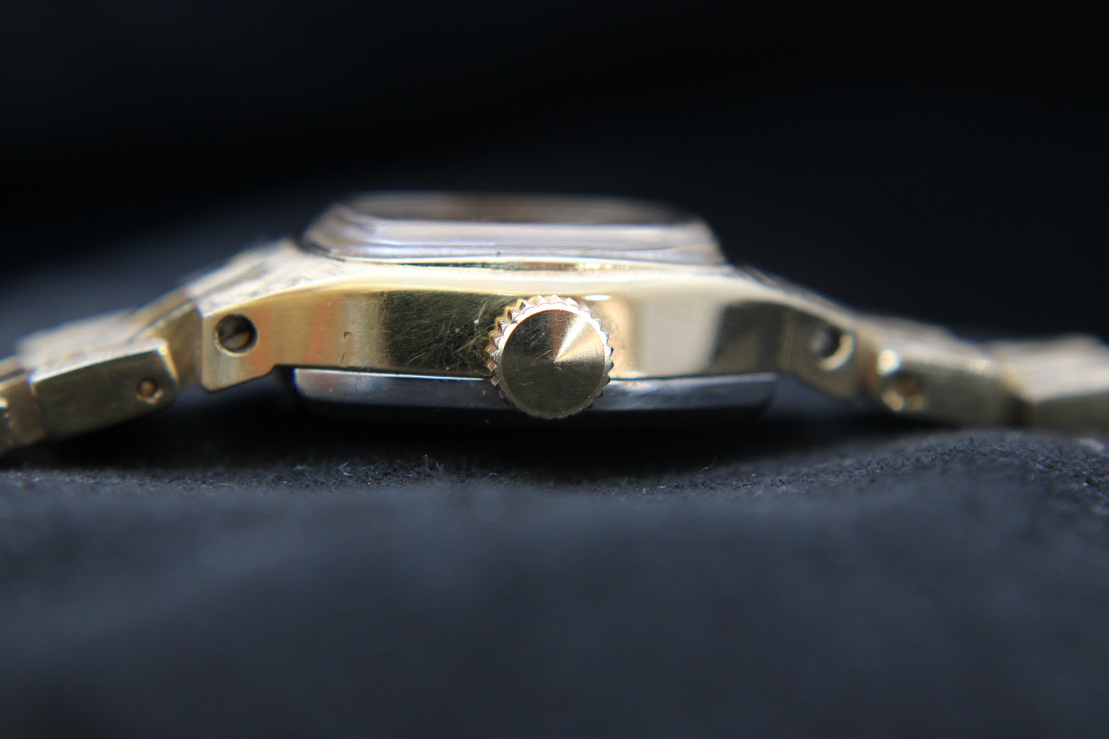 Side view of the watch crown on the right, showing its textured gold finish and case profile.