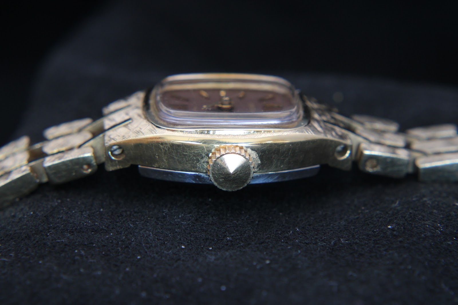 Angled side view of the watch crown, showing minor wear on the gold-tone case.