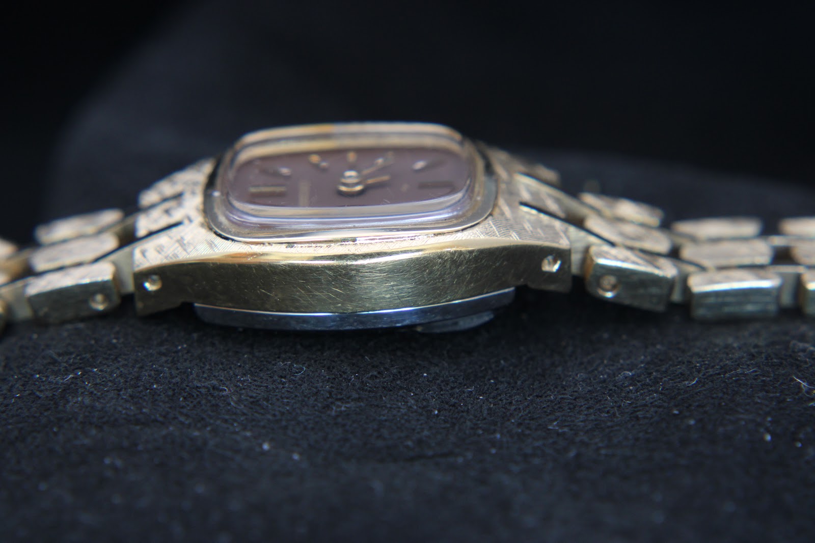 Left side view of the watch case, showing the textured gold-tone finish and slim profile.