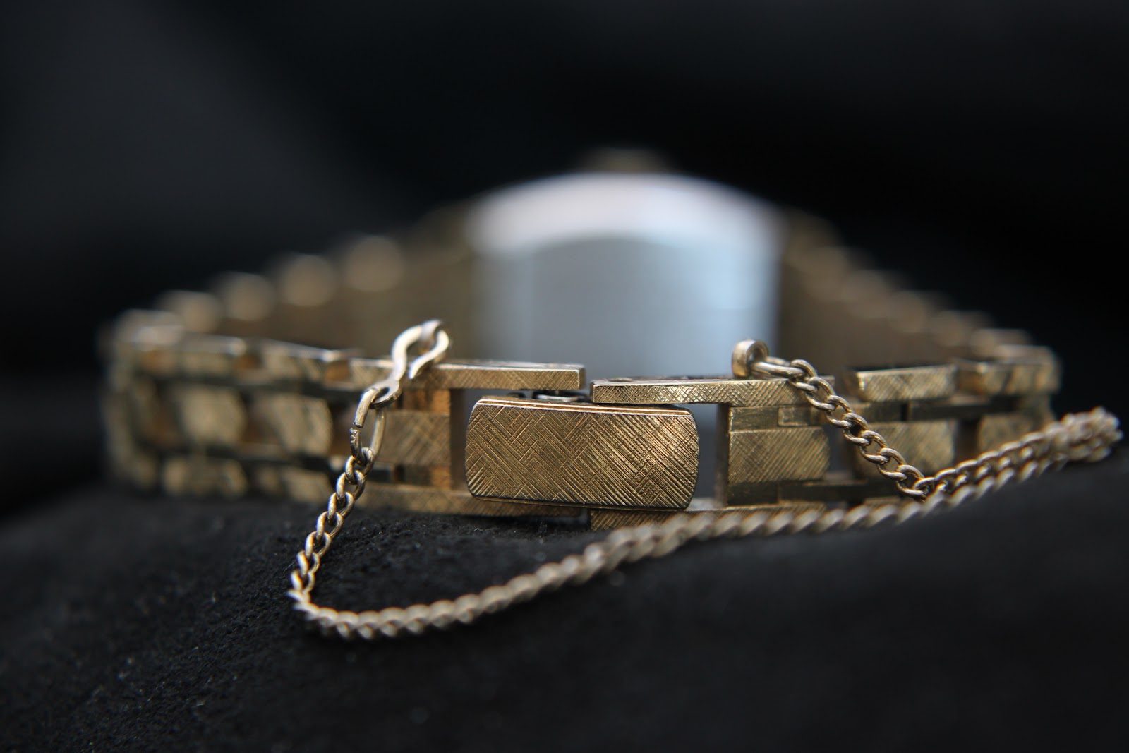 Close-up of the integrated gold-tone bracelet clasp with a safety chain, showing textured links.