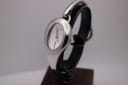 Angled front view of the Gucci 103 watch on a display stand, showing the silver teardrop case and dial.