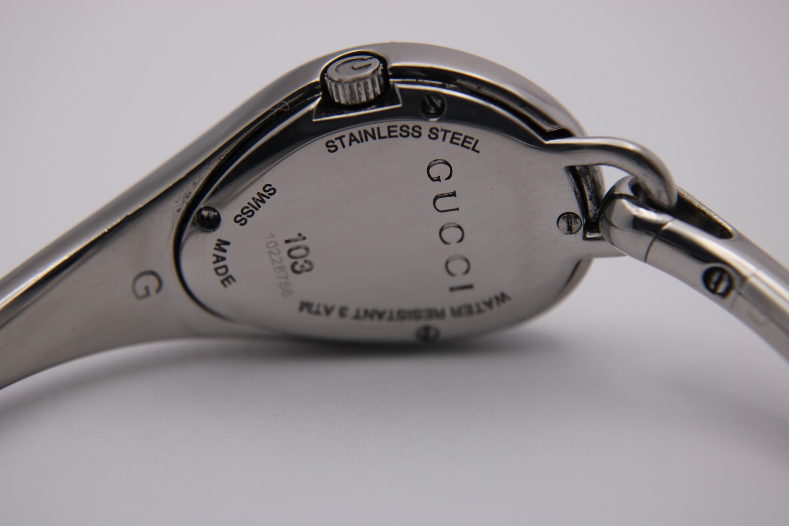 Close-up of the watch case back, showing 'GUCCI', 'STAINLESS STEEL', 'SWISS MADE', '103', '10228756', and 'WATER RESISTANT 3 ATM'.