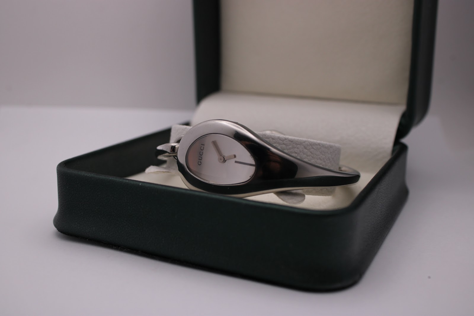Angled view of the Gucci 103 watch resting inside a dark green presentation box with white interior.