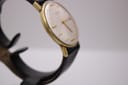 Another angled side view of the Magna watch, focusing on the left side of the gold-tone case and lug area.