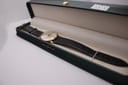 The Magna 21 jewels watch with its black leather strap, presented inside a dark green watch box, viewed from an elevated angle.