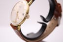 Side view of the Magna watch on a display stand, showing the ribbed crown and the gold-tone case profile.