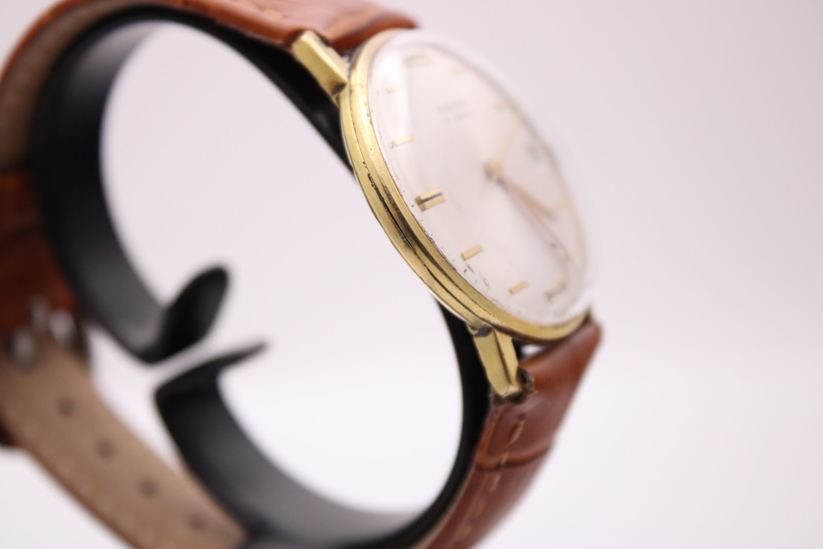 Angled side view of the Magna watch, highlighting the domed crystal and the elegant profile of the gold-tone case.