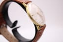 Angled side view of the Magna watch, highlighting the domed crystal and the elegant profile of the gold-tone case.