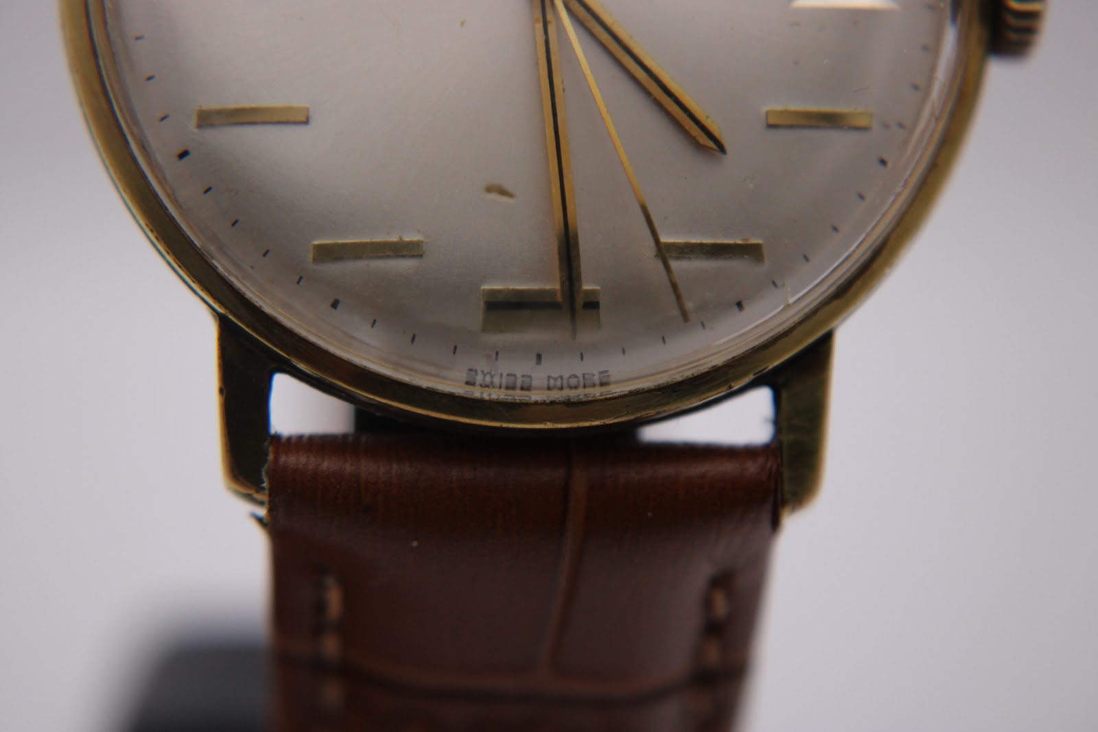 Extreme close-up of the lower part of the Magna watch dial, revealing 'SWISS MADE' text and the connection point of the brown leather strap.
