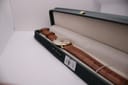 The Magna 21 Jewels watch with its brown leather strap laid out inside an open dark green presentation box, against a white background.
