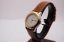 Angled side view of the Tissot PRX P340-G on a dark watch stand, showing the two-tone case and brown leather strap.
