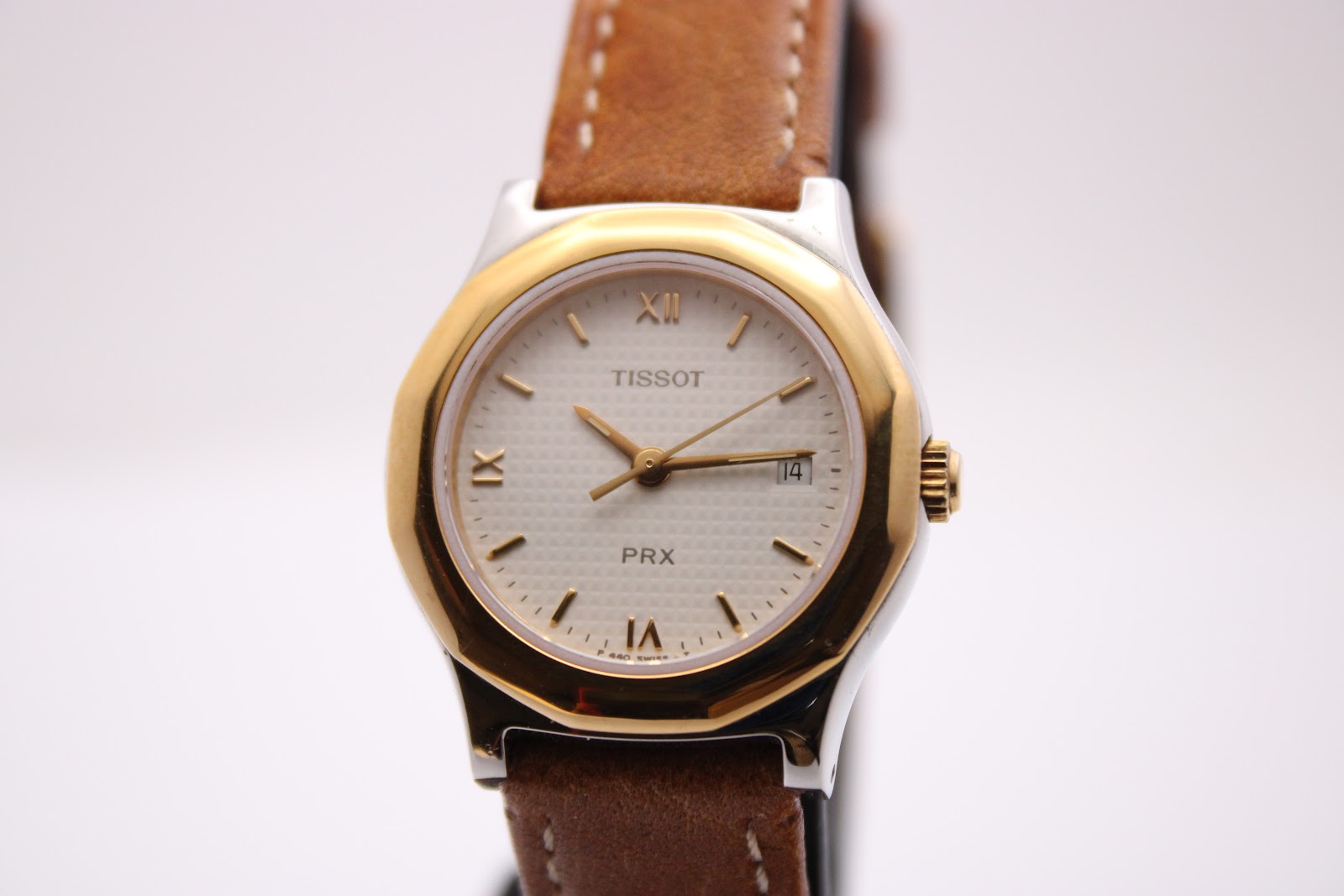 Front view of the Tissot PRX P340-G on a dark watch stand, highlighting the white textured dial with gold-tone Roman numerals.