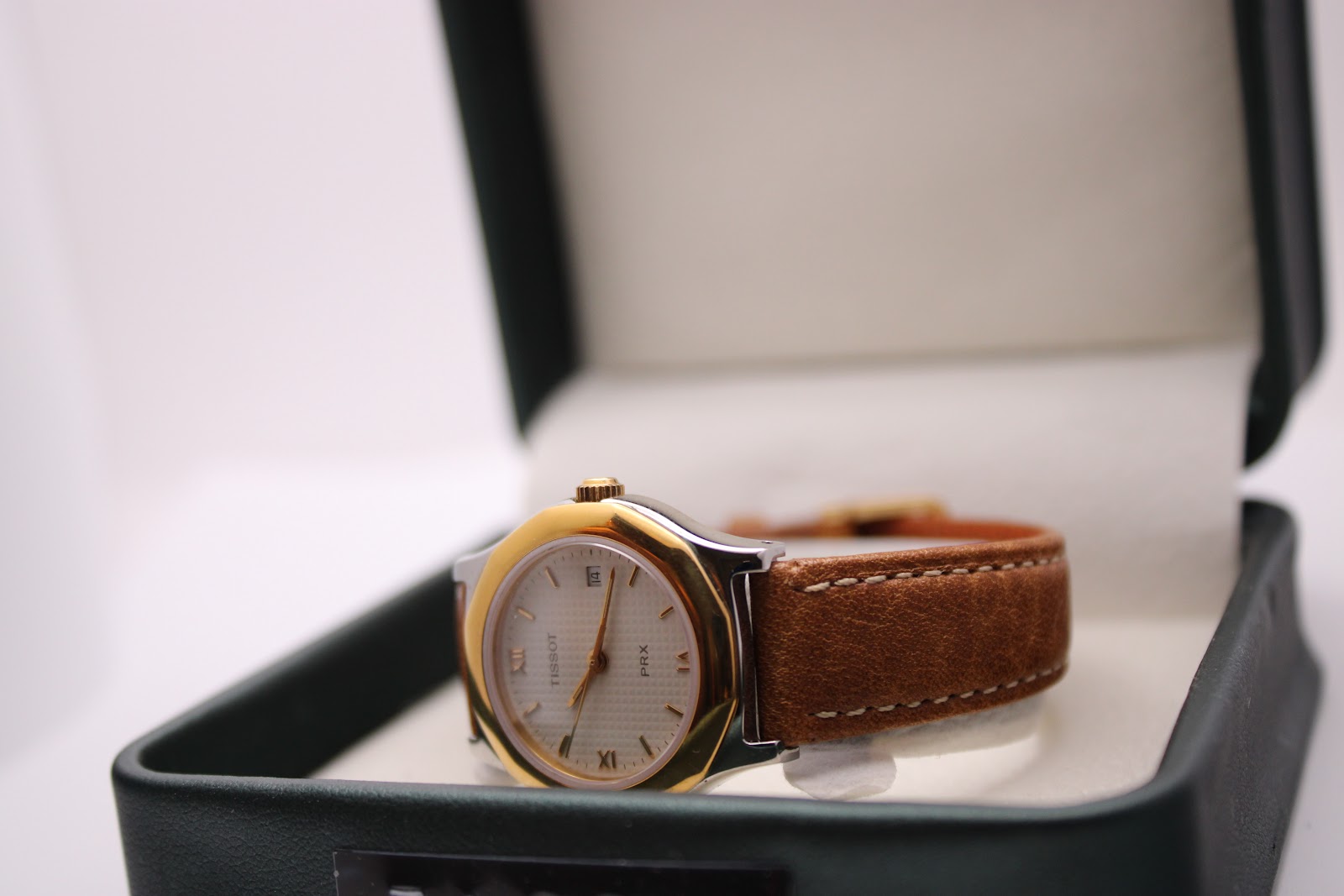 Tissot PRX P340-G resting in a dark green presentation box, with the dial facing upwards.