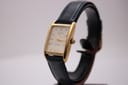 Angled view of the Tissot Fascination gold-tone rectangular watch with a navy leather strap on a watch stand.