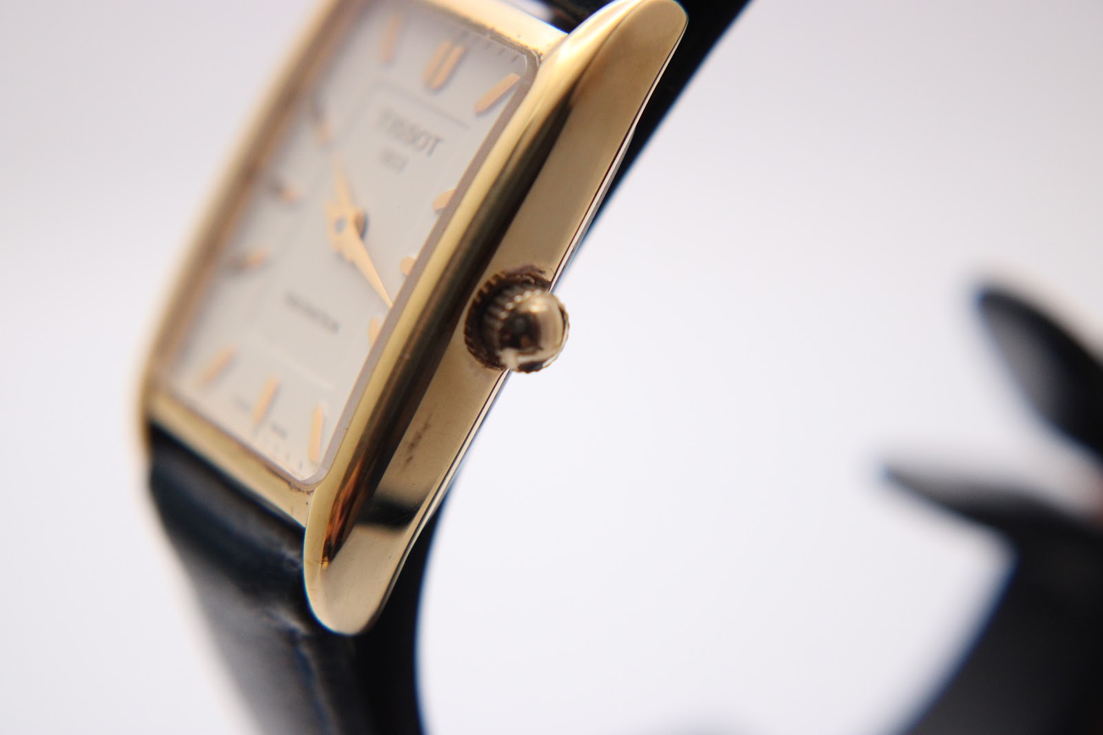 Close-up side profile of the Tissot watch's polished gold-tone rectangular case and fluted crown.