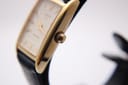 Close-up side profile of the Tissot watch's polished gold-tone rectangular case and fluted crown.