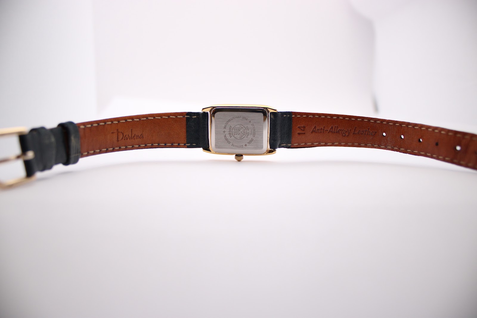 Overhead view of the Tissot watch with the navy leather strap unbuckled, showing inner strap markings 'Darlena' and '14 Anti-Allergy Leather'.