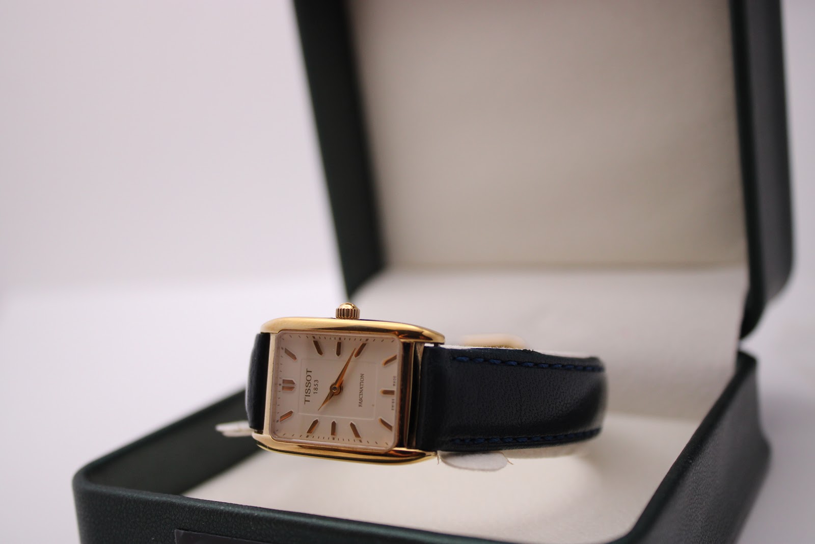The Tissot Fascination watch resting on an open dark green presentation box, displaying its dial and strap.