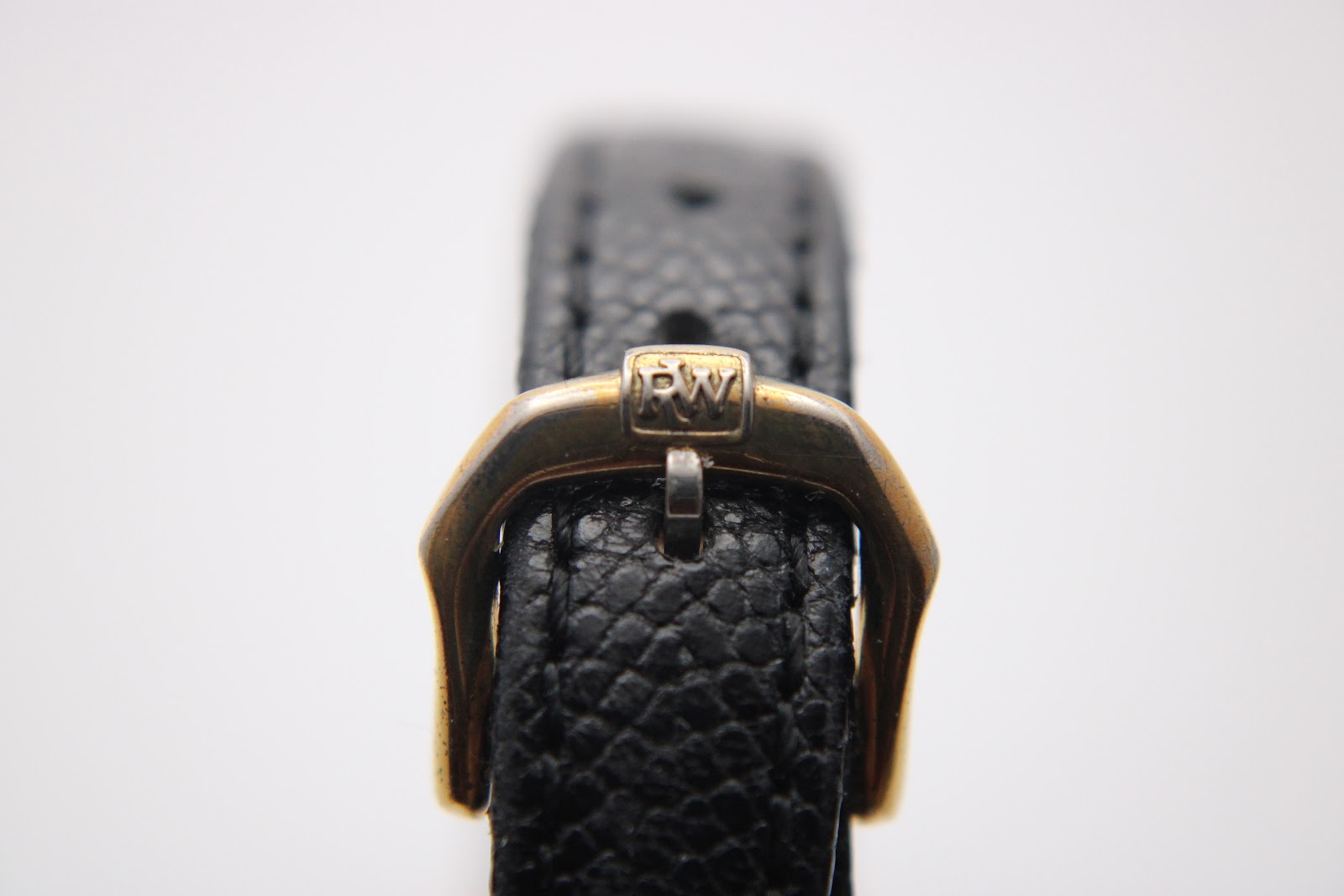 Close-up of the gold-tone buckle on the black textured leather strap, clearly showing the embossed 'RW' logo.