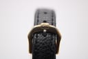 Close-up of the gold-tone buckle on the black textured leather strap, clearly showing the embossed 'RW' logo.