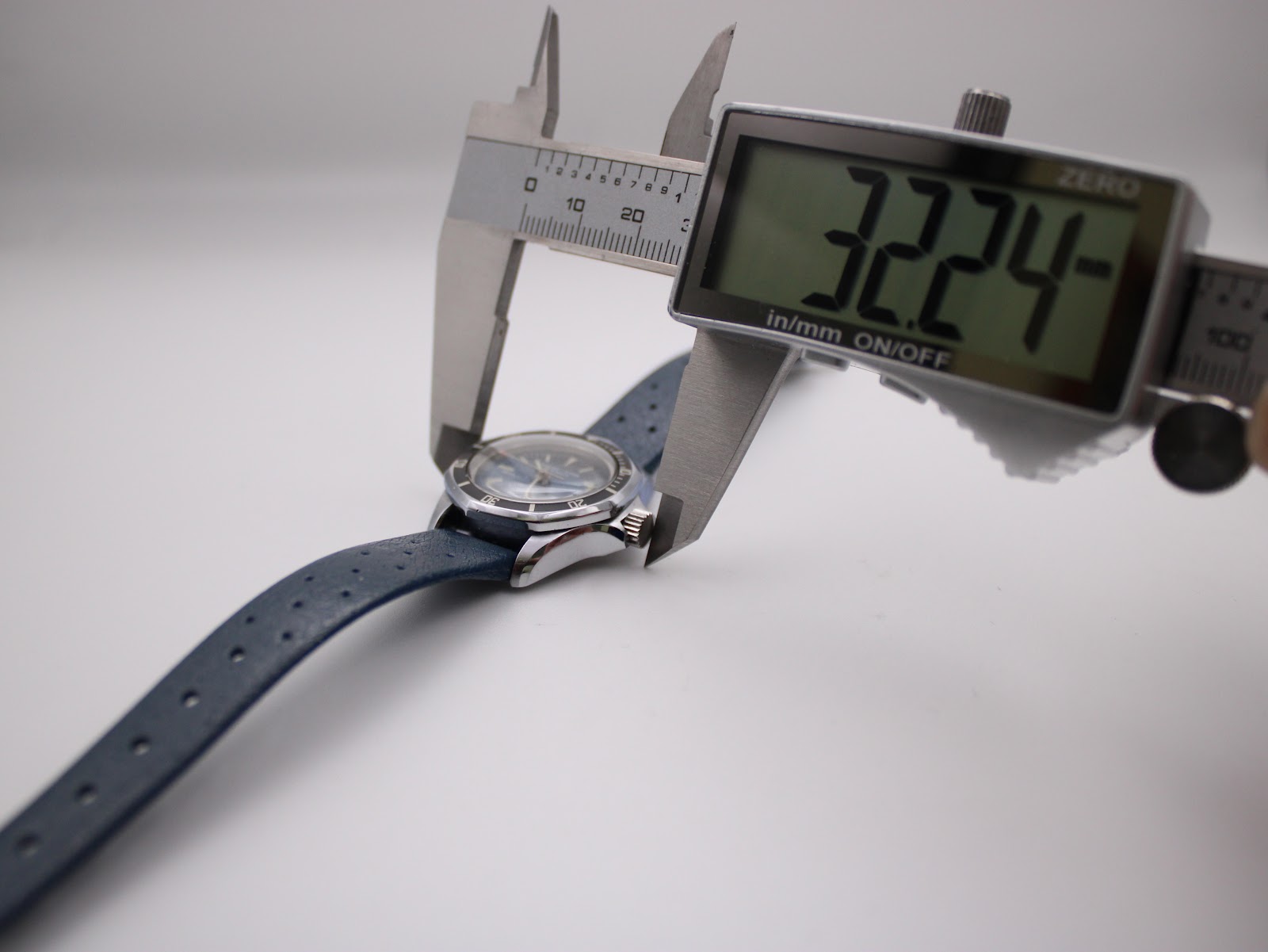 Digital caliper measuring the watch case including the crown, displaying a measurement of 32.24mm.