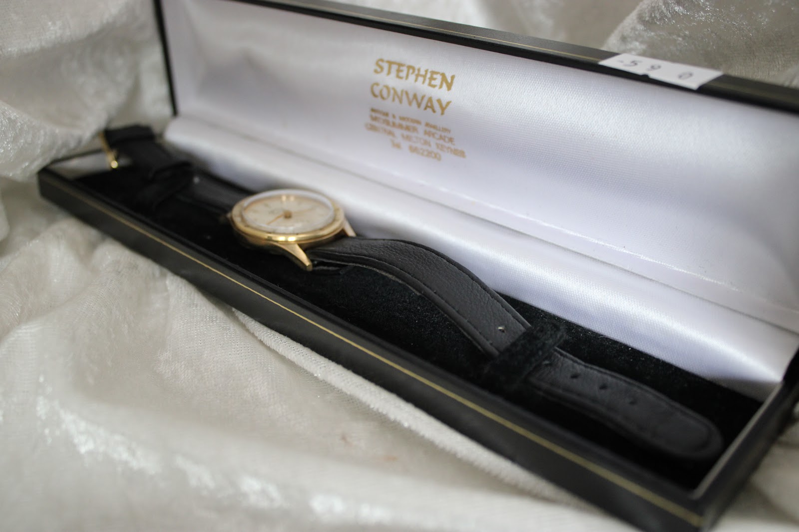 Overhead view of the gold-tone Services Marine watch with black leather strap resting inside an open Stephen Conway presentation box.