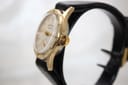 Side view of the Services Marine watch on a display stand, highlighting the textured gold crown and the profile of the case.